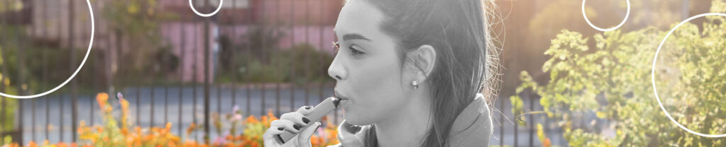 mulher de cabelo preso fumando pod descartável em um jardim